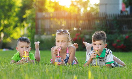 childs drink juice on the grass childs drinks fresh orange juice from jars and cocktail straws outdoor. little boys and girls are having fun on a sunny day. family summer holiday conceptの写真素材