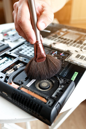 Repaiman with brush is cleaning disassembled laptop parts. Technical support and fixing gadgets problems. Servicing, repairing, cleaning, maintaining computers. repair shop. hardware maintenanceの写真素材