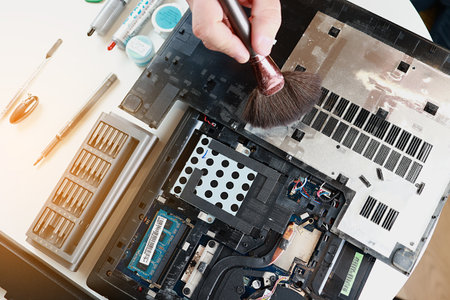 Repaiman with brush is cleaning disassembled laptop parts. Technical support and fixing gadgets problems. Servicing, repairing, cleaning, maintaining computers. repair shop. hardware maintenanceの写真素材