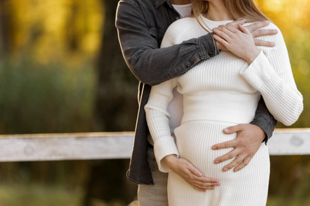 Happy stylish pregnant woman and man hugs, kiss, touches belly and listen babys kicks, walk outdoor...