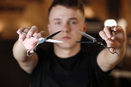 Barbershop. Unrecognisable hairdresser is holding two type of scissors. Barber professional tools. Male haircut, fashion. Hair salon, haircut and shaving background. Small business. Selective focus.の写真素材