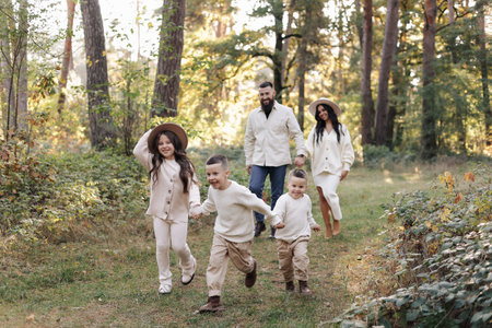 Young mother, father with daughter and sons are walking, having fun in autumn forest. Family holding...