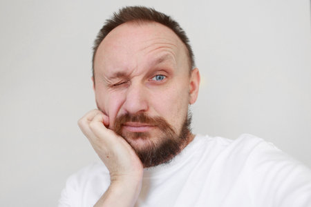 shot mans hand is unrestrained scratching unshaven chin. Overgrown unkempt male in white t shirt with thick beard and mustache face. Beauty salon concept, barbershop.の写真素材