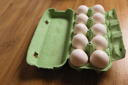 Dozen white fresh chicken eggs in the green cardboard egg tray on wooden table background. Fresh organic eggs in open carton pack or egg container. nutritional food. Farm's products concept.の写真素材
