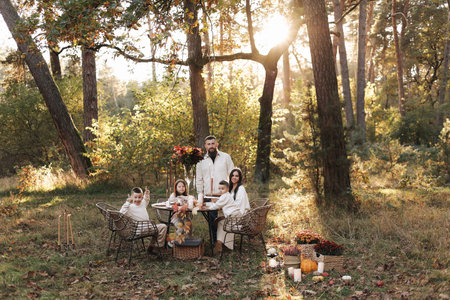 Happy family day. Young dad, mom, child daughter, two little sons, big dog have picnic and sitting by the table in autumn park. children day. Concept of family coziness, relationships, communication.の写真素材