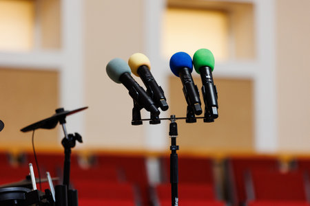 Four colored microphones on stand on podium and a lot of red chairs blurred in the background. Concept of communication, event, seminar, media, press conference, performance, politics, companyの写真素材