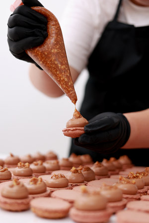 Close up of chef hands putting salt caramel with nuts in ganache cream on chocolate macarons shells. Macaroon Baking Concept. Cooking, Food And Baking Concept. Confectionery And Baking Conceptの写真素材