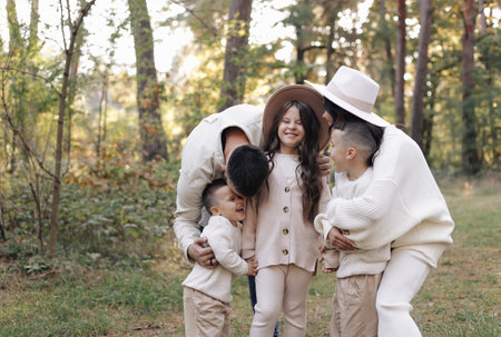 Young mother, father with daughter and sons are walking, having fun in autumn forest. Family holding hands enjoying time together at background of trees. happy parenting and childhood conceptの写真素材