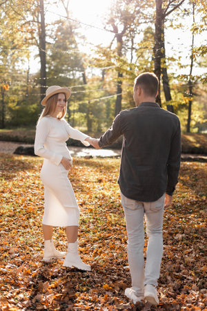 couple, man and pregnant wife are holding hands and walking in the autumn park on sunset. Happy family enjoying pregnancy on nature. The concept of Mother's Day and Women's Dayの写真素材