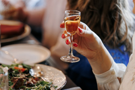 Unrecognizable woman holding glass of alcohol drink, cognac, liquor makes toast by the festive table, fun for a birthday, wedding, anniversary or any other holiday, happy atmosphere, friendly company.の写真素材
