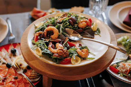Close up festive table with fresh salad with grill seafood, greens and tomatoes on plate on wooden...
