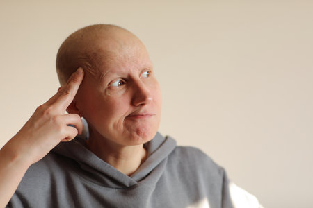 Face expressions and emotions. Thoughtful bald female is wearing casual sweatshirt at home holding hand on head, having doubtful look, looking side. health problems, cancer, alopecia. copyspace.の写真素材