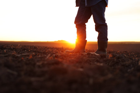 agriculture. Cropped shot of view businessman farmer in rubber boots walks along plowed field. Agronomist checking and analyzes fertile soil on sunrise. Agribusinessの写真素材