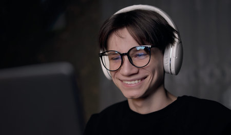 Young gamer man in glasses with screen reflection and headphones streaming live action game while...