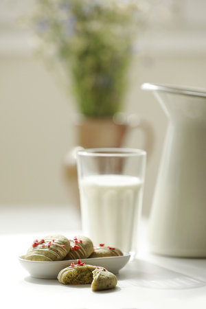 Composition with homemade mint gingerbread cookies with matcha and sublimated strawberries in plate, glass of milk, jug and wild flowers in vase on background.Sugar, gluten and lactose free and vegan.の写真素材