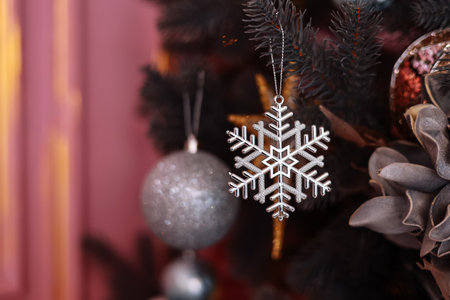 Close up view of Christmas tree branches with stylish shiny silver snowflake, glitter baubles or balls, modern ornaments on pink wall background. New 2024 year holiday celebration. Copy space.の写真素材