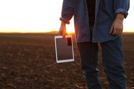 agriculture. Cropped shot of back view businessman farmer in rubber boots walks along plowed field with digital tablet. Agronomist checking and analyzes fertile soil on sunrise. Agribusinessの写真素材