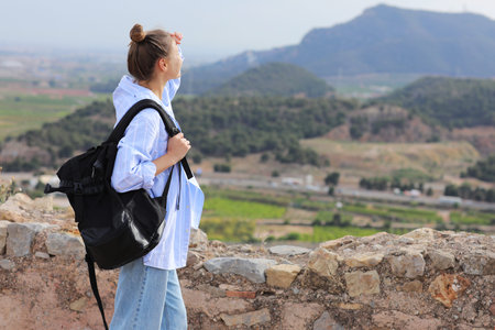 Back view of young hiker woman with backpack on the hill looking and relaxing at mountains and...