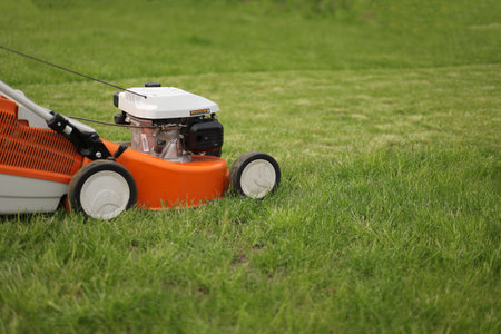 Close up orange-grey electric lawn mower on bright lush green lawn. gardening work tools. Rotary lawn mower machine cut grass. Professional lawn care service. Place for text.の写真素材