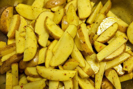 Slices of fresh raw potatoes in peel with spices on a baking sheet. Potato wedges in oil and herbs ready for baking in a rustic way, close up. Preparing healthy vegan mealの写真素材
