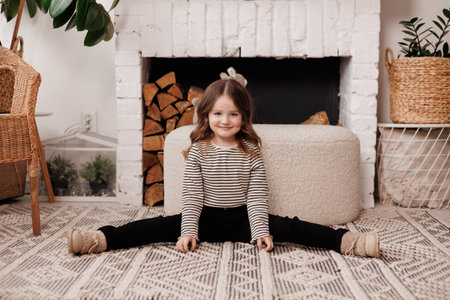 Playful adorable preschooler little child girl in casual clothes having fun sits on twine at living room in rustic style. Concept of happy childhood, emotions, education, lifestyle, facial expression.の写真素材