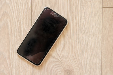 Smartphone with a broken touch screen, glass with cracks on wooden background. Mobile phone display...