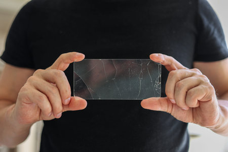 Broken protective glass for smartphone touch screen in hands of phone repairman on black background....