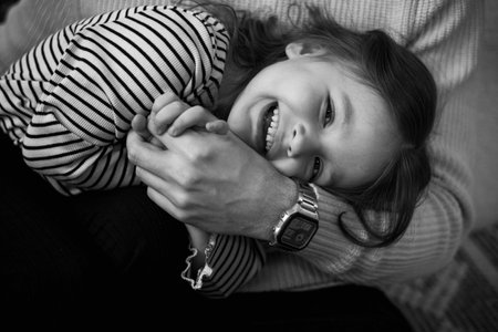 Happy childrens day. Black and white photo of unrecognisable dad with adorable laughing little daughter are having fun spending time together on weekend at home. Playful child girl and daddy hugging.の写真素材