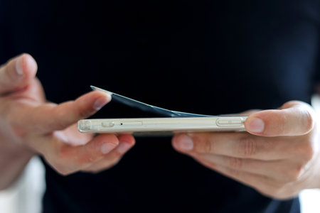 Process unrecognizable repairman is removing broken and old tempered glass screen protector from smartphone, close up view. Services for gluing and replacement of damaged protective glassの写真素材
