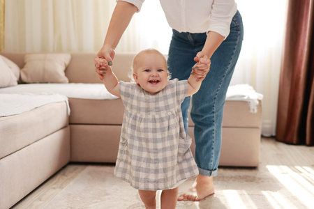 smiling baby boy girl learning to walk with mom, taking first steps with mother helping infant,...