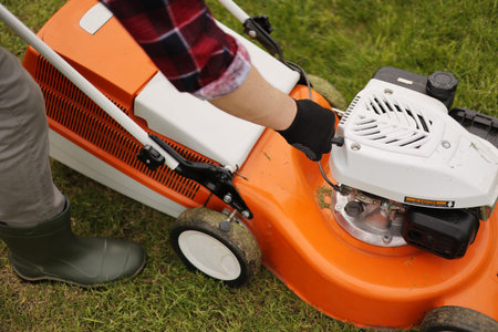 Unrecognizable gardener man in protective gloves starts the lawnmower before cutting green grass...