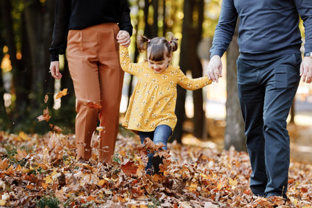 family day. Happy young mom, dad and little child daughter having fun playing with fallen yellow...