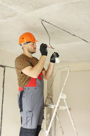 Electric in uniform, protective gloves and hard hat checking and measuring the presence of...