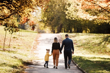family day. Happy smiling dad and mom having fun with their child daughter outdoors at autumn park. Couple lifting their cheerful girl kid up by the hands, enjoying nature and walking. children's day.の写真素材