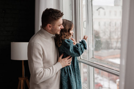 Fathers day. Happy loving young dad embracing adorable little daughter by the window at home. Happy...