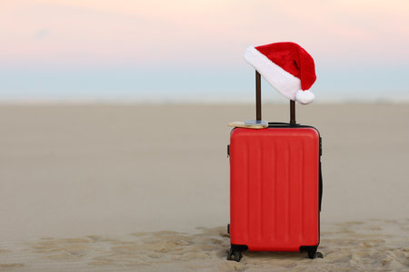 Red suitcase with Santa Claus hat, smartphone and passport on tropical sand beach and sea backdrop. Travel on Christmas and New Year winter holidays concept. Last minute trips, hot tours. Copy space.の写真素材