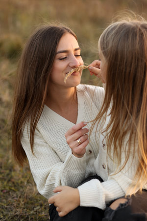 Family day, mother's day. Happy smiling young mom and adorable child daughter soft hugging, kissing and spending time together at autumn on sunset. Idyllic family having fun outdoors on fall holidayの写真素材