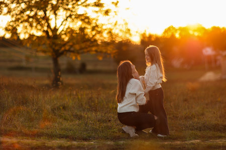 Family day, mother's day. Happy smiling young mom and adorable child daughter soft hugging, kissing and spending time together at autumn on sunset. Idyllic family having fun outdoors on fall holidayの写真素材