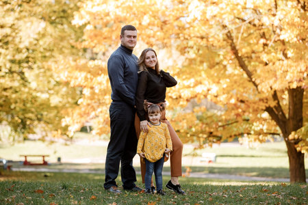 Family day. Happy young mom and dad hold their little child daughter hands walk, have fun outdoor at autumn park, enjoy spend time together at weekend.Parental love, mental health and happy lifestyle.の写真素材