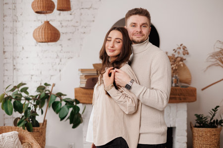 Happy young couple in love is hugging gentle and smiling together celebrating Valentines day at cozy Scandinavian style home. Man and woman enjoying spending time together, relaxing on dateの写真素材