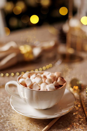 Vintage classic white porzellan cup with saucer with cocoa and marshmallow on golden glittering tablecloth. Christmas or New Years festive party luxury table setting. Garland lights bokeh on backdropの写真素材
