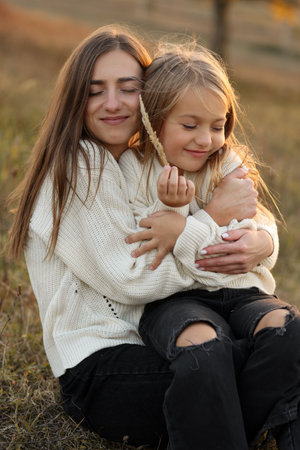 Family day, mothers day. Happy smiling young mom and adorable child daughter soft hugging, kissing and spending time together at autumn on sunset. Idyllic family having fun outdoors on fall holidayの写真素材