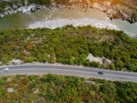 Aerial drone view of rocky canyon Moraca river with big stone boulders, asphalt road with moving cars, Montenegro. Vibrant lush green vegetation in summer. Popular travel destination.の写真素材