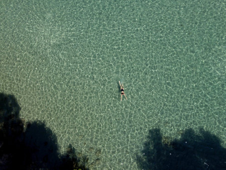 Above view of woman swimming at sea. Aerial top view of young girl in white swimsuit floating on water surface in crystal clear turquoise sea. Vacation at Paradise. Ocean relax, travel and vacation.の写真素材