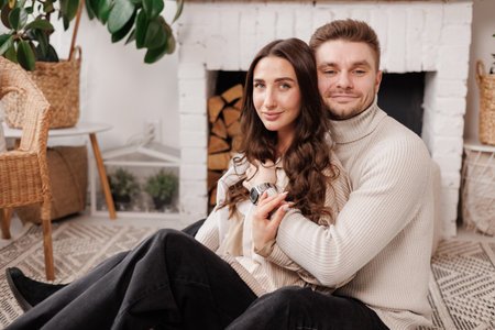 Happy young couple in love is hugging gentle and smiling together celebrating Valentines day at cozy Scandinavian style home. Man and woman enjoying spending time together, relaxing on dateの写真素材