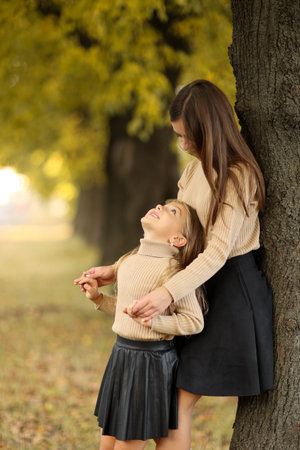 Family day. Young mom and little daughter having fun and enjoy relaxing outdoors in autumn park. Adorable child girl tightly hugs and kisses her mother. Maternal care and love for kid. Mothers day.の写真素材