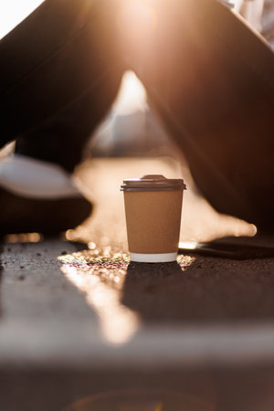 Craft paper cup with recycling plastic lid, mock up, place for text. Unrecognisable man sits outdoors, relaxes with takeaway hot drink on background, sunlight. Coffee break, to go.Zero waste concept.の写真素材