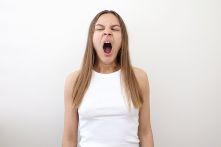 Caucasian young woman yawning and covering wide open mouth with hand isolated on white background. Girl looking sleepy and tired, exhausted for fatigue, lazy eyes in the morningの写真素材