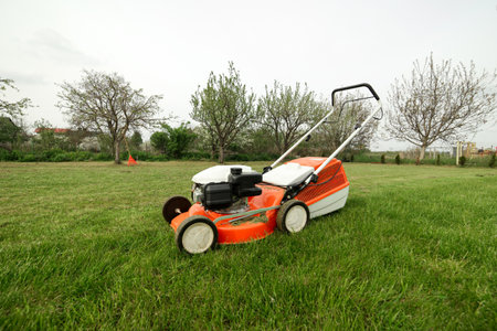 Top view of modern orange-gray gasoline lawn mower cutting bright lush green grass. Gardening work tools. Rotary lawn mower machine on lawn. Professional law care service. Place for text.の写真素材