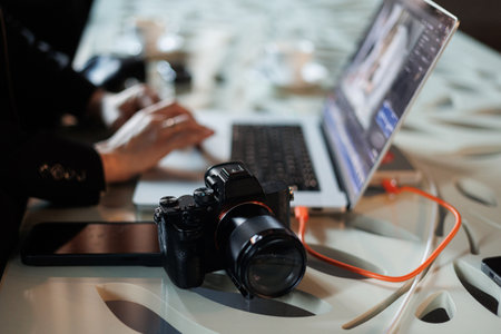 Workspace with laptop and photo camera. Unrecognisable female photographer works, sends photos from dslr camera on computer through cord at workplace by table. Creative artist lifestyle.の写真素材